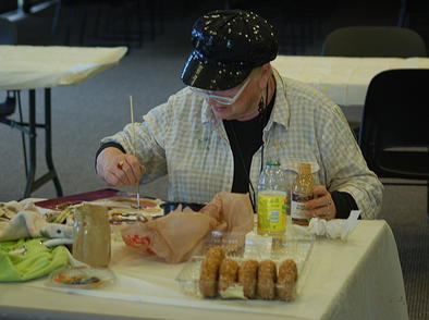 A woman paints on a table with donuts in front of her. 